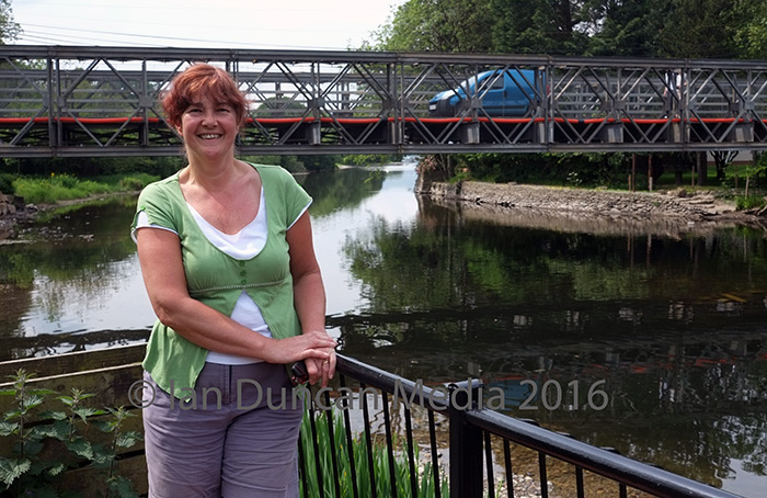 BUILDING BRIDGES... Mandy Watson, who runs Pooley Bridge post office, beside the replacement crossing which reconnects the village for local people and visitors...
